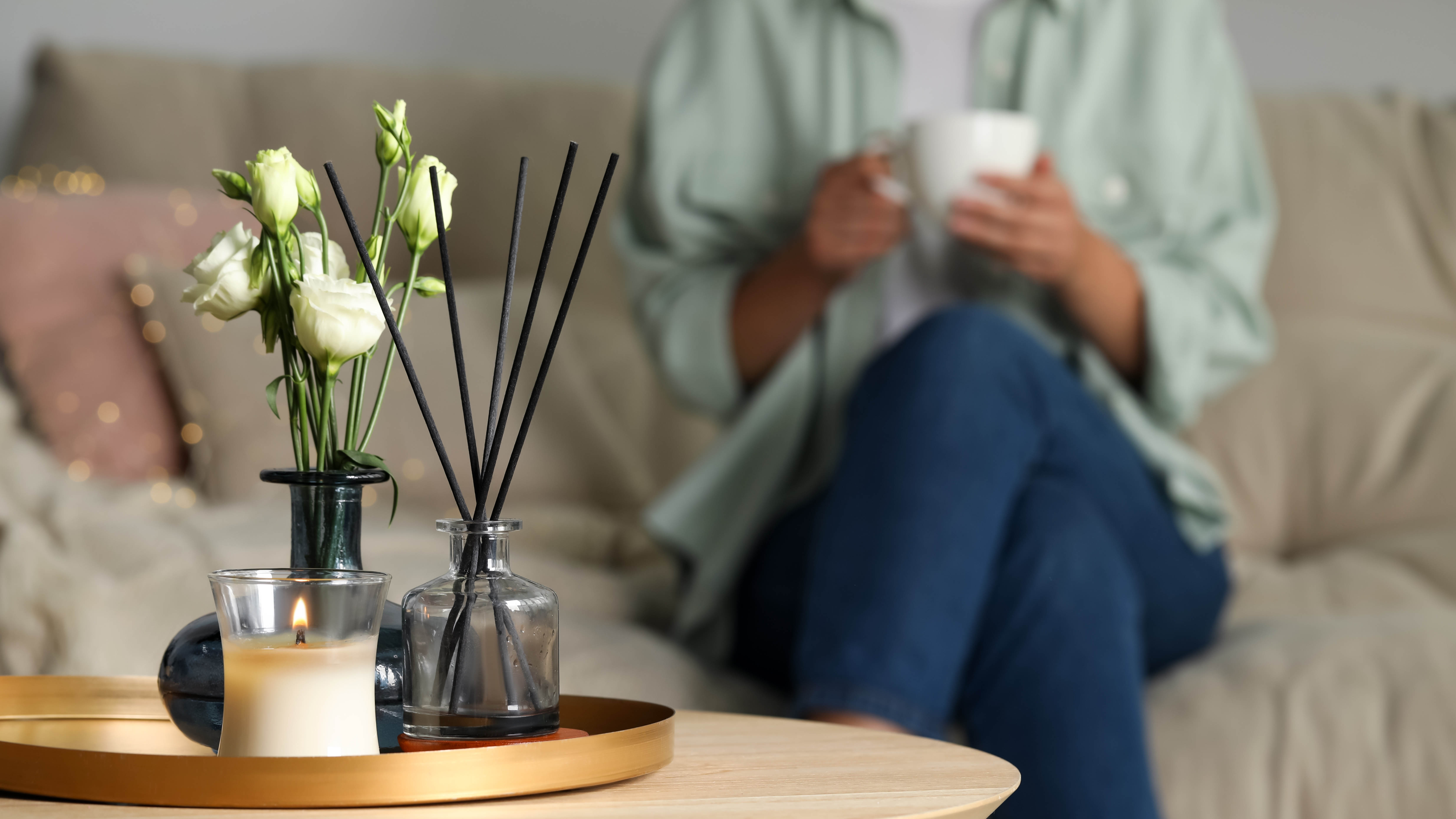 Candle and diffuser on coffee table with women seated on sofa holding a white mug