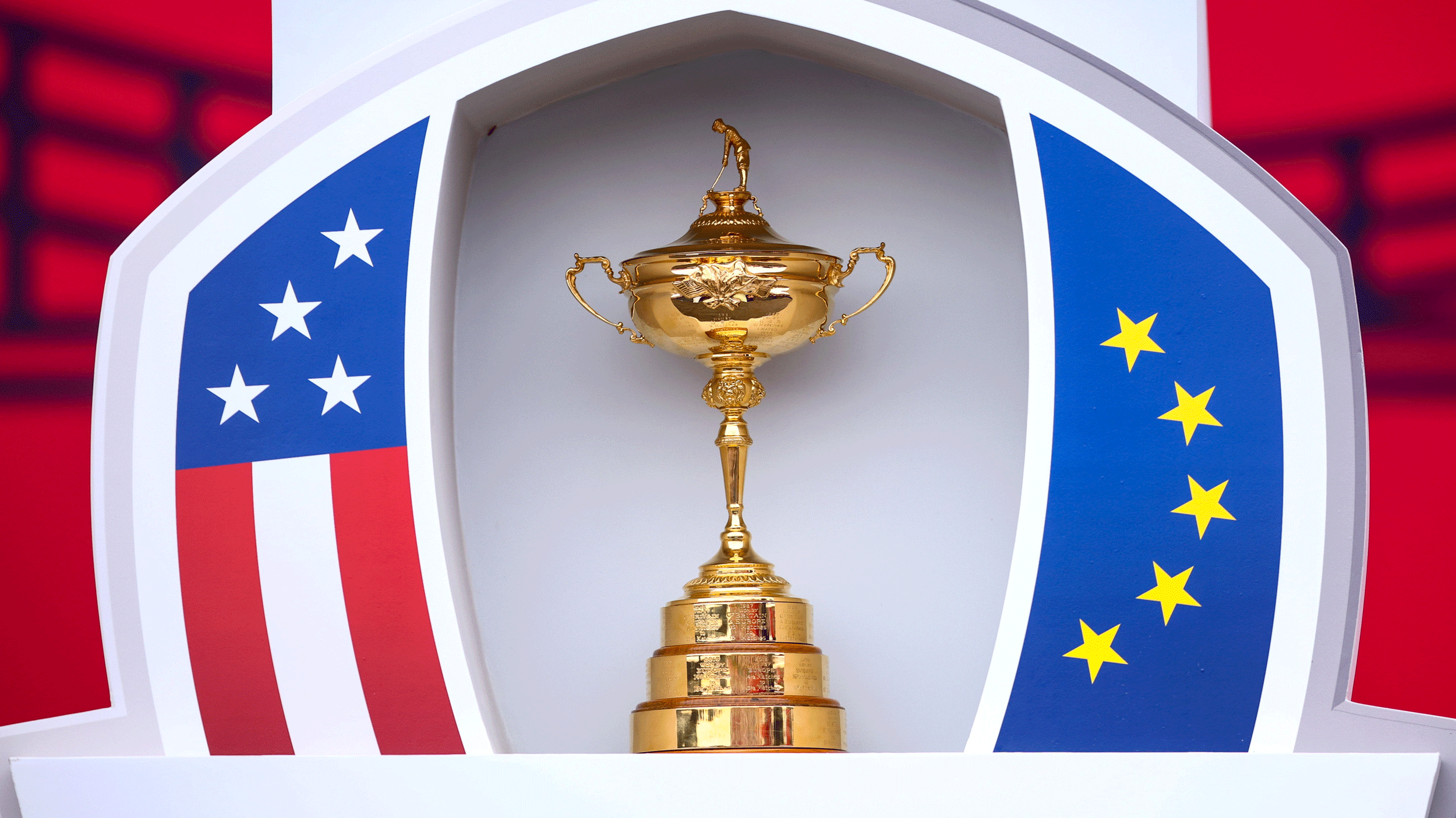 The Ryder Cup sits in between an American flag pattern (left) and a European flag pattern (right)