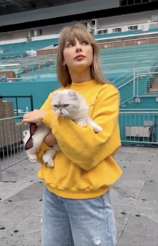 Taylor Swift wears a yellow sweatshirt and baggy jeans while standing in the Hard Rock Stadium in Miami