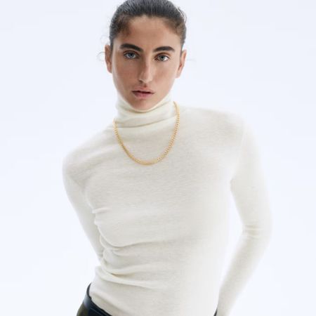 Woman wears cream turtleneck top, gold necklace