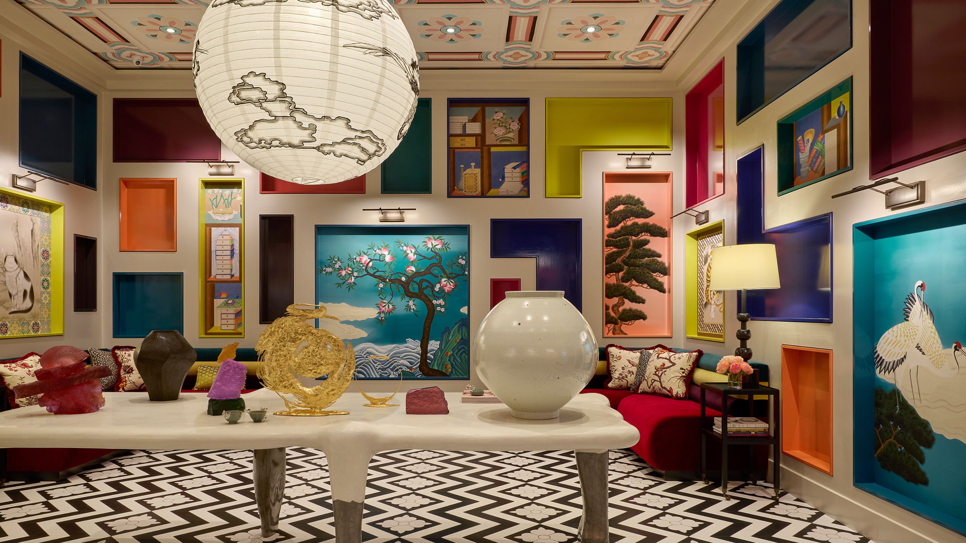 A vibrant, eclectic room featuring walls filled with colorful, recessed display niches showcasing art. Includes a bold black-and-white chevron floor, unique sculptures, and a large paper lantern.