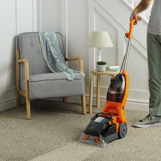 Vax carpet cleaner being used on a carpet in a hallway next to a chair and staircase