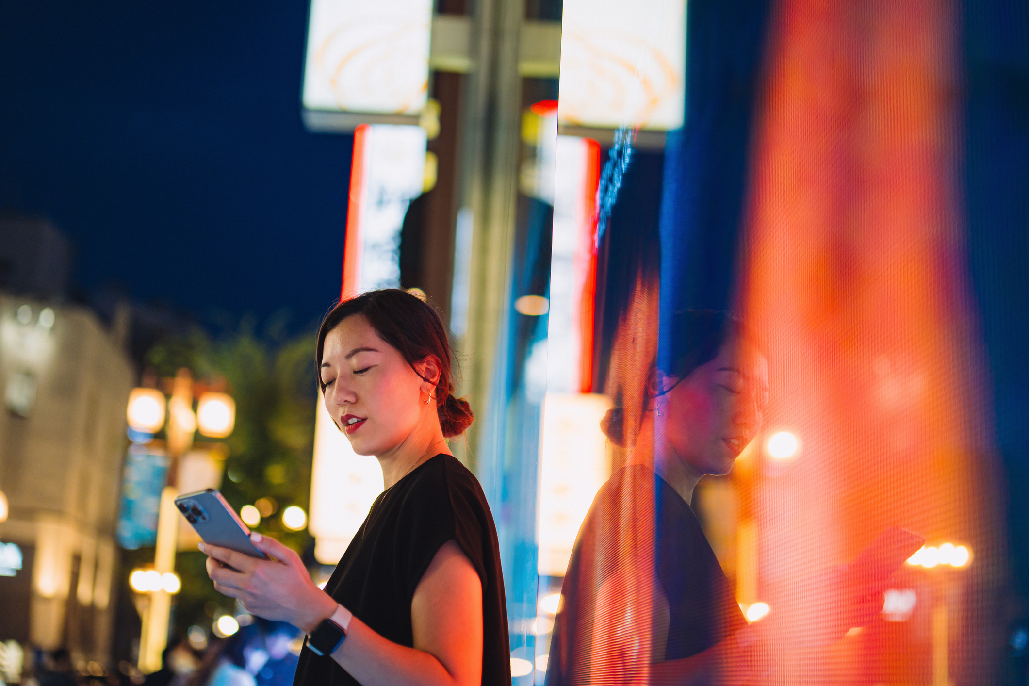 Young woman using smartphone, discovering AI while walking on city street at night 