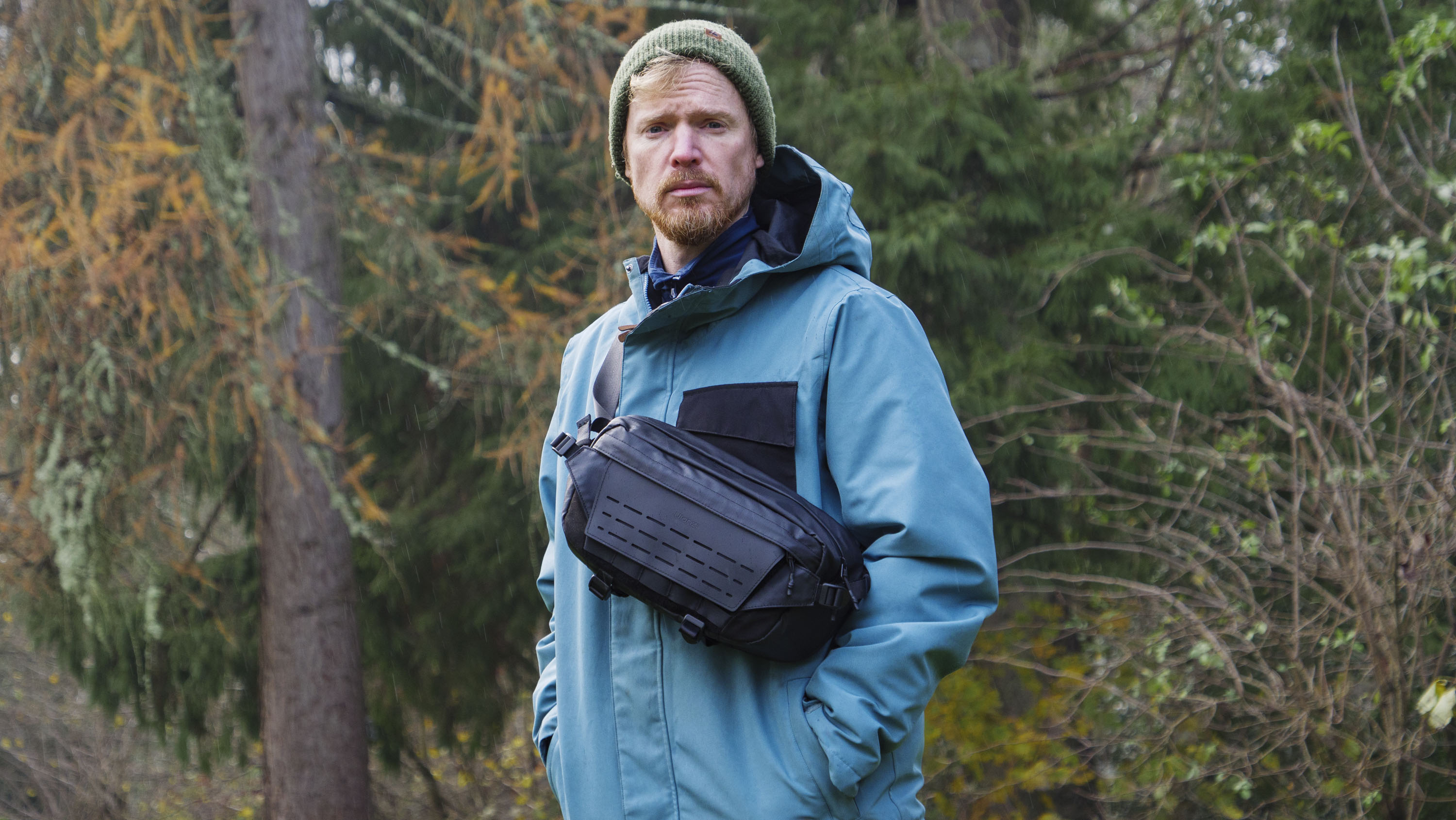 Man wearing a blue jacket outside with a Ulanzi Camera Sling Bag over his shoulder and resting on his midriff