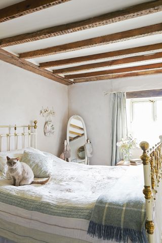 bedroom with brass bedstead and beams and cat on bed