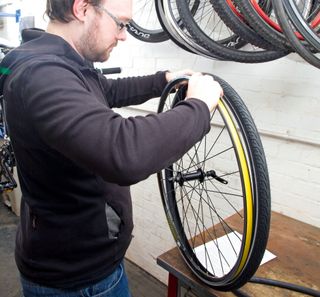 fix a puncture mend an inner tube shows a person in a black hoodie on the left of the image reseating a tyre on to a wheel
