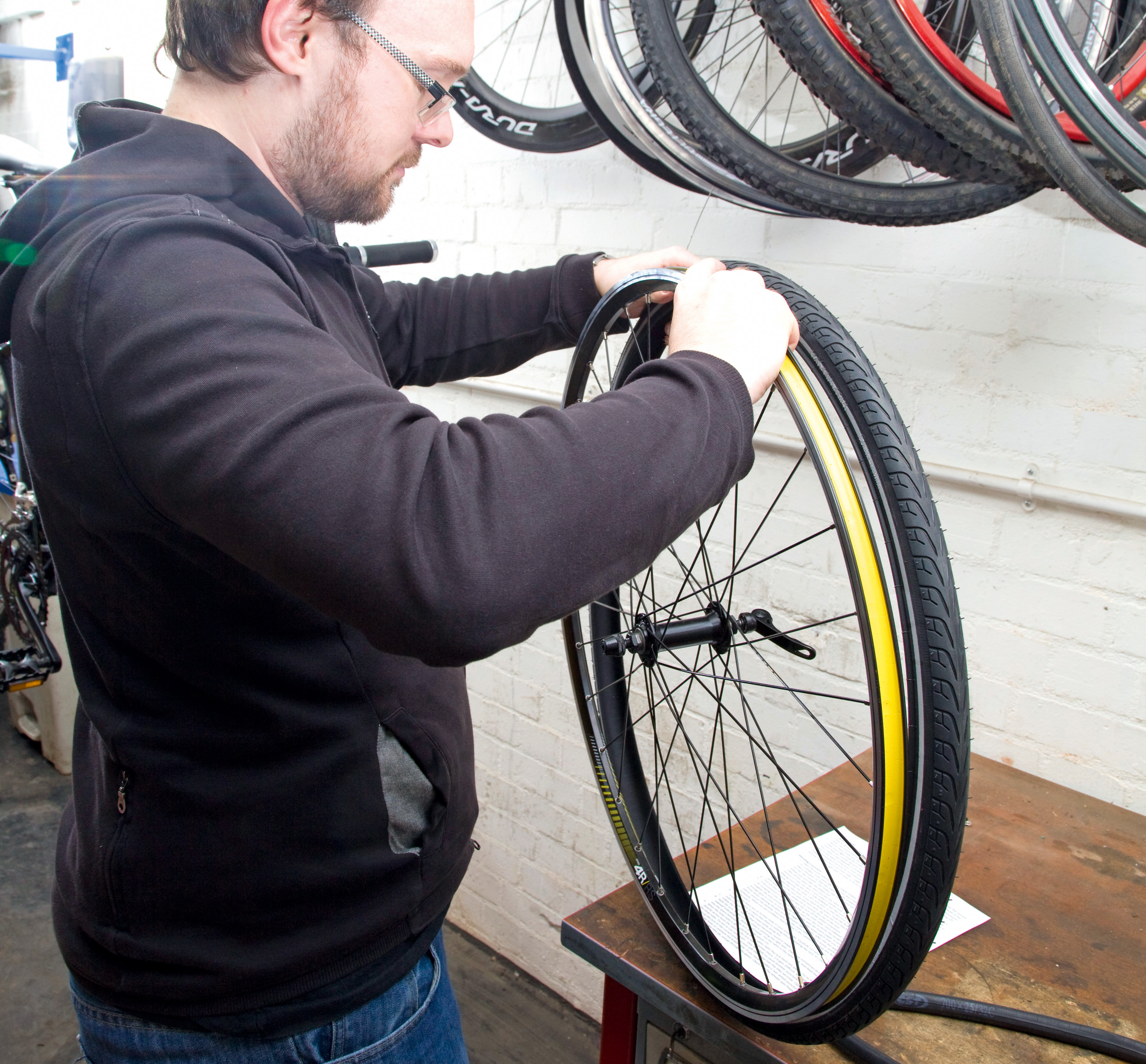 fix a puncture mend an inner tube shows a person in a black hoodie on the left of the image reseating a tyre on to a wheel