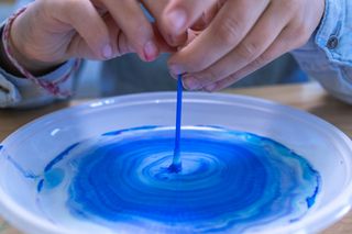 Close up of girl's hands using a cotton bud while doing colour changing milk experiment in the laboratory.