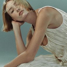 Model leaning her head on her hand with her elbow on her knee, wearing a ruffled cream strap dress from Nordstrom Rack. 