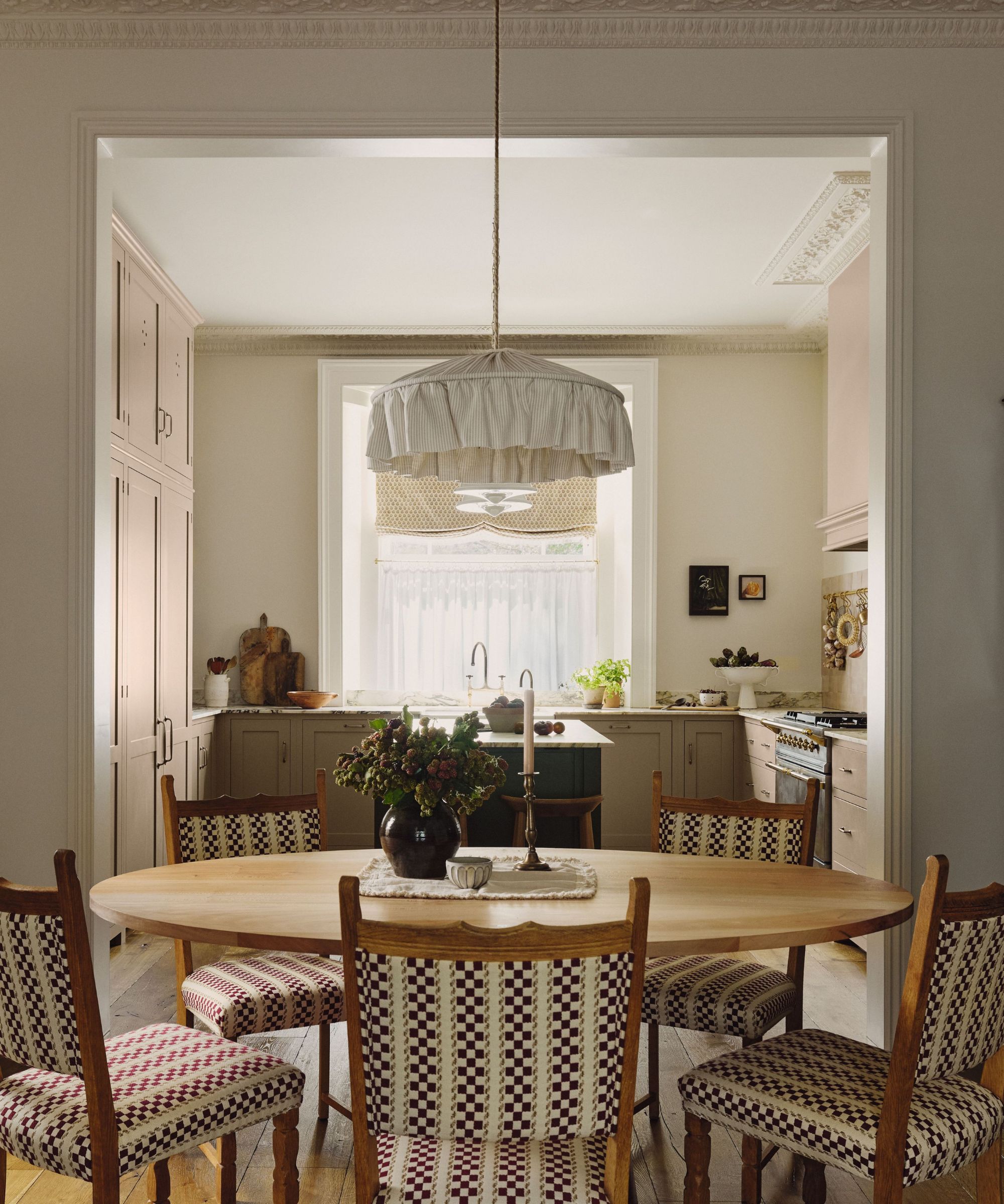 Breakfast table with bistro chairs, round wooden table, low pleated pendant light looking into the kitchen