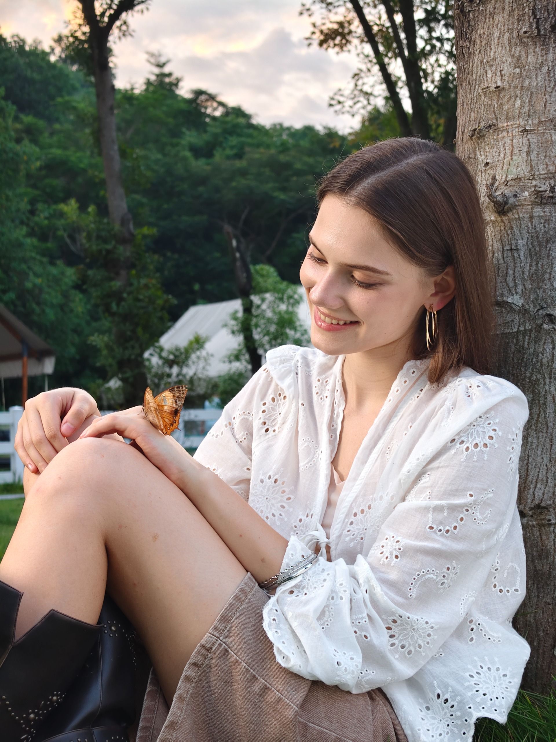A woman sitting on the ground with a butterfly on her arm