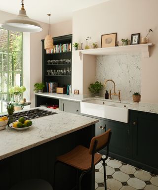 Dark green and white kitchen with marble, hob in island, bar stool, butler's sink, brass faucet