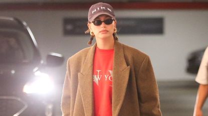 Hailey Bieber in red micro shorts, a red sweatshirt, and tan maxi coat