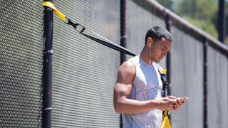 A man access the TRX app on his phone to find a workout to do with the TRX Home2 System suspension trainer