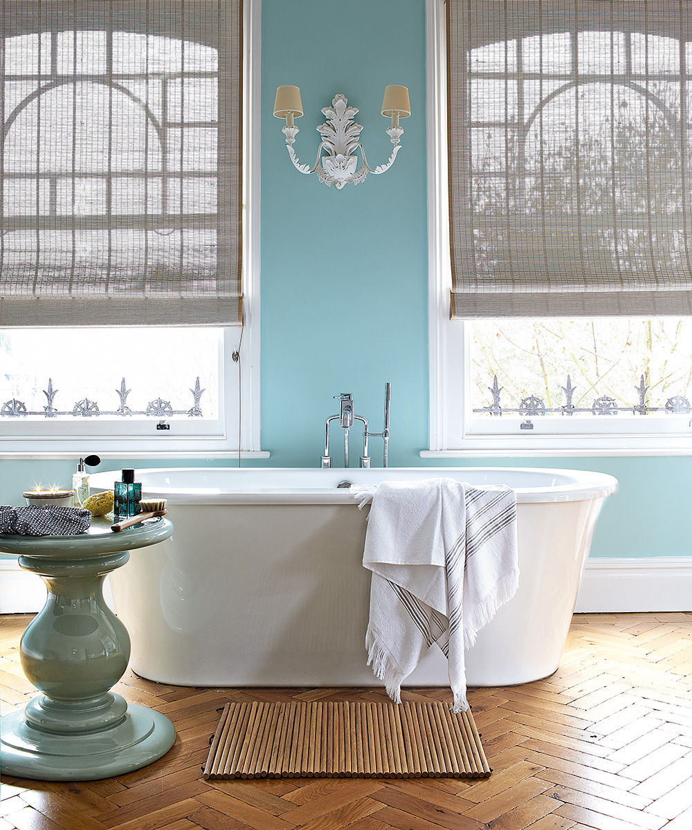 An example of bathroom paint ideas showing a white bath in a bathroom with parquet flooring, blue walls and two windows