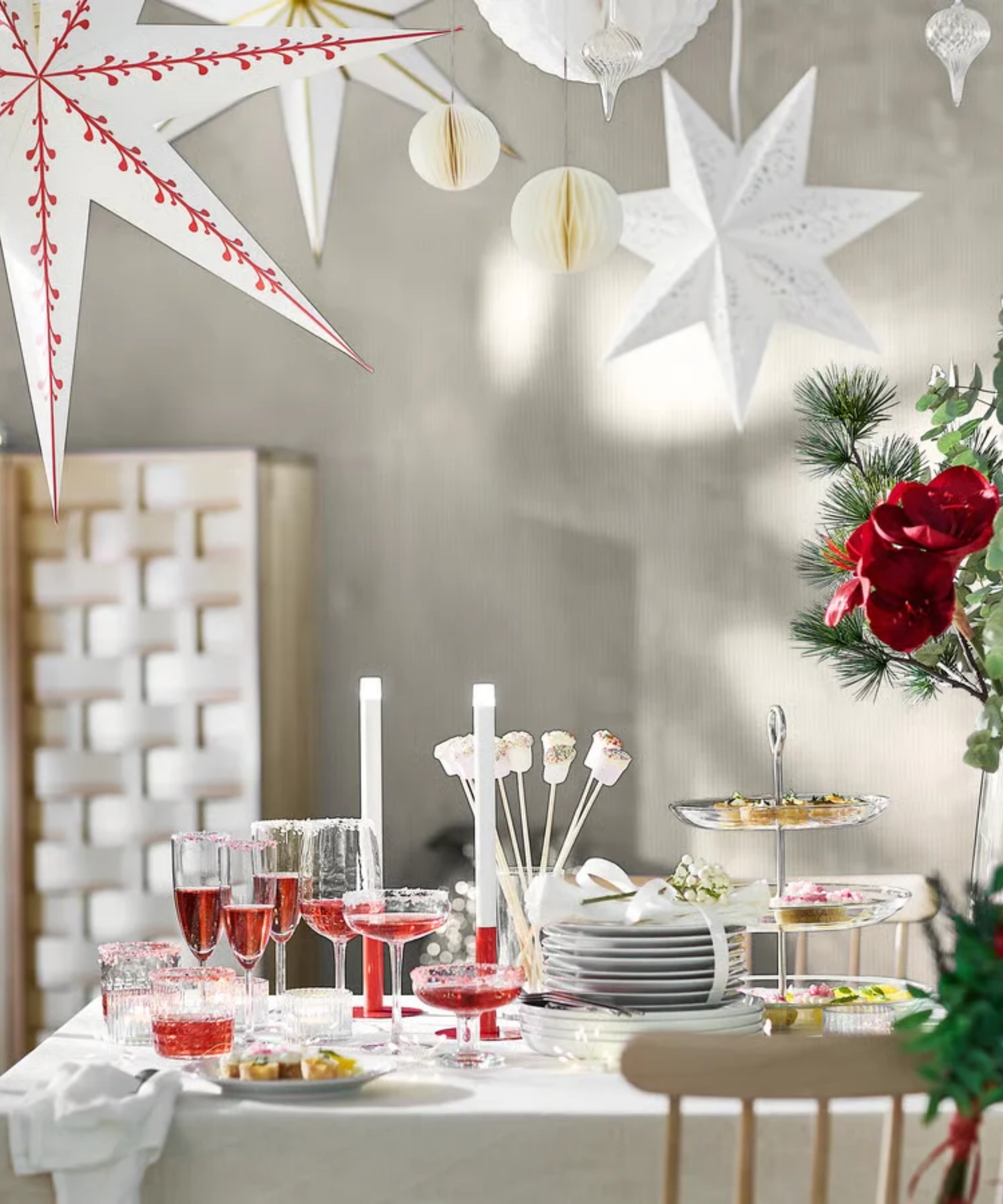 IKEA star-shaped Strala lantern lights hanging overhead a minimalist holiday dining room area with bright red florals and winter foliage