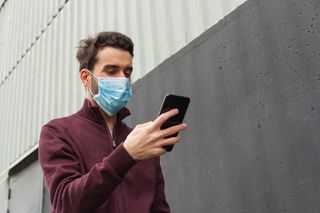 A man wearing a medical mask checks his phone.