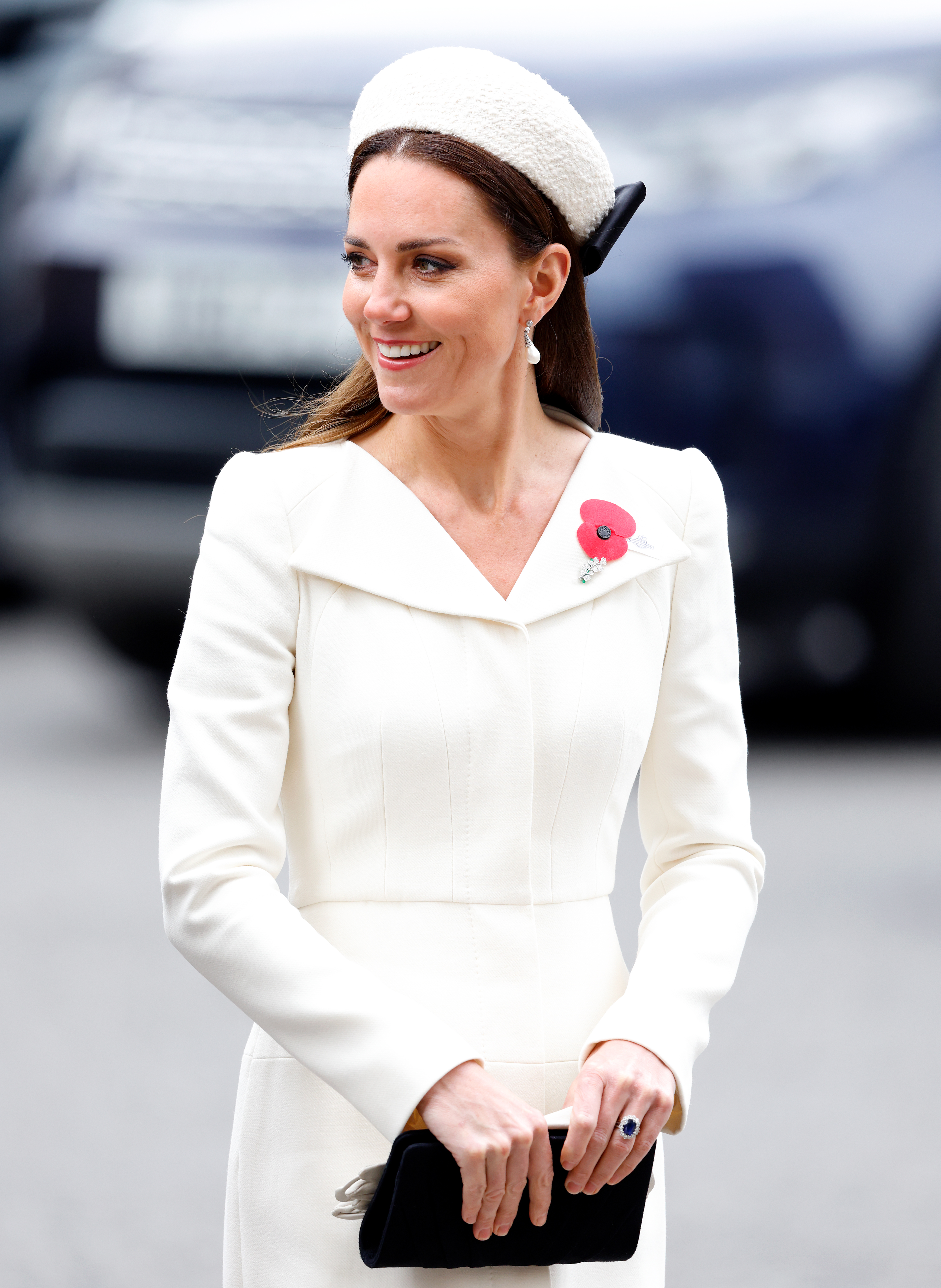 Princess Kate wearing a white dress and hat smiling and holding a purse