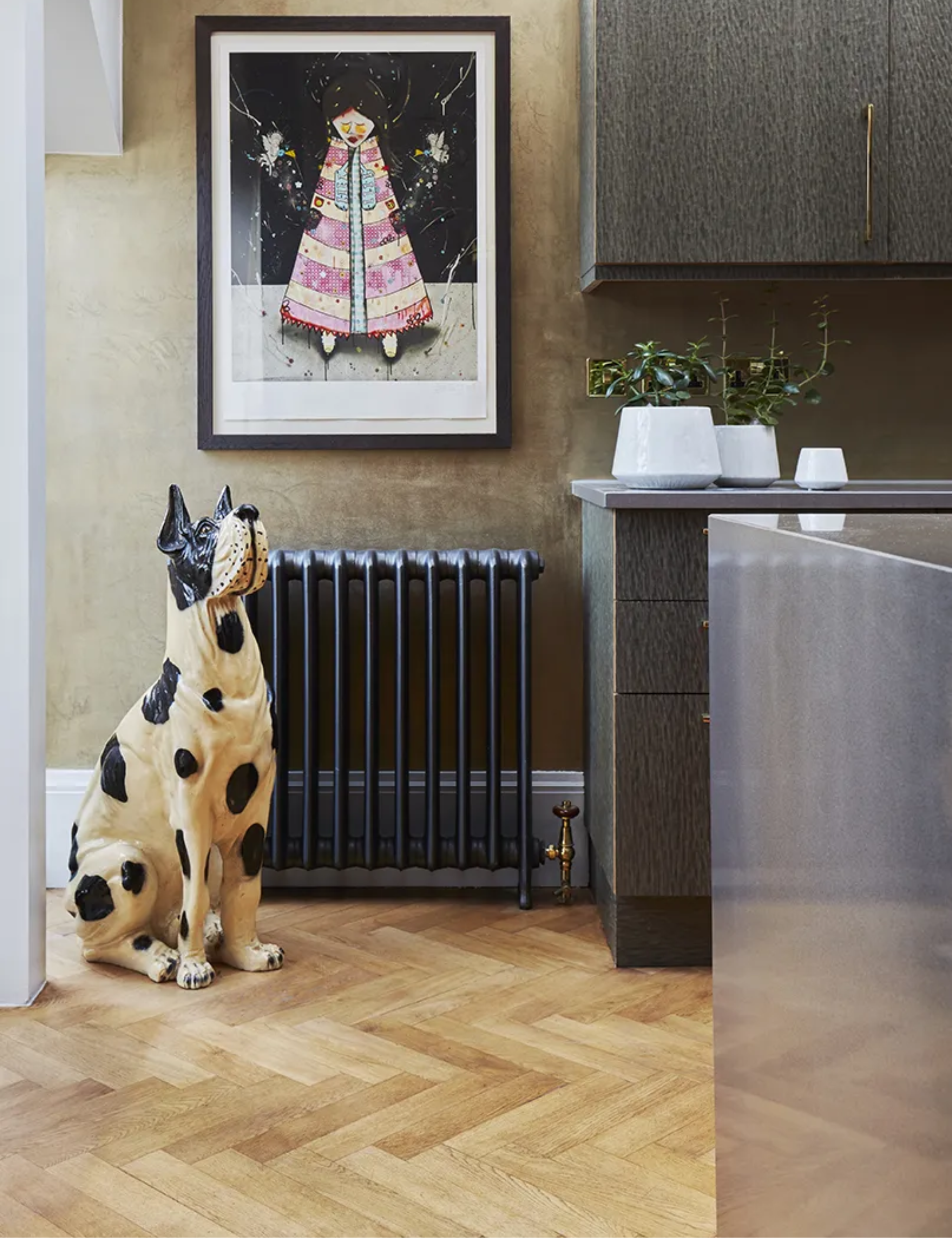 A kitchen with gray slab cabinets, a vintage radiator, and a ceramic dog statue on wooden herringbone flooring
