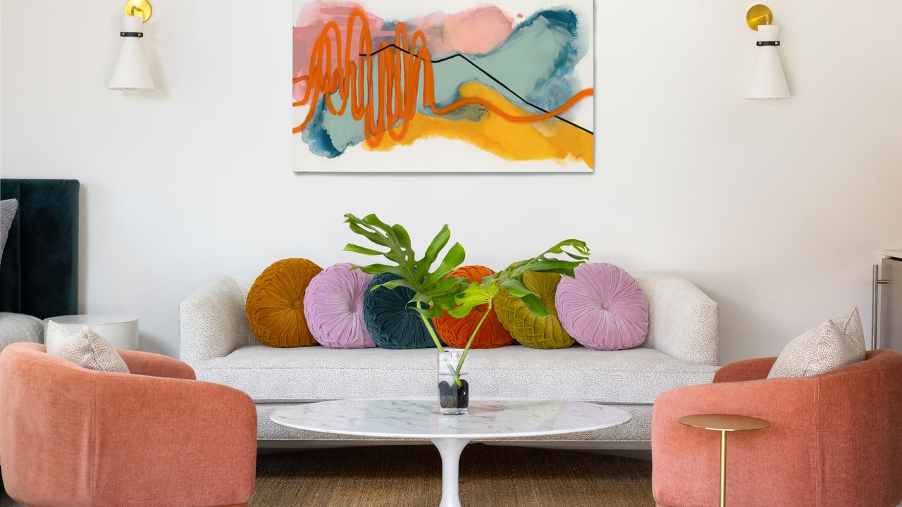 Small living room with white sofa, coral armchairs and abstract artwork