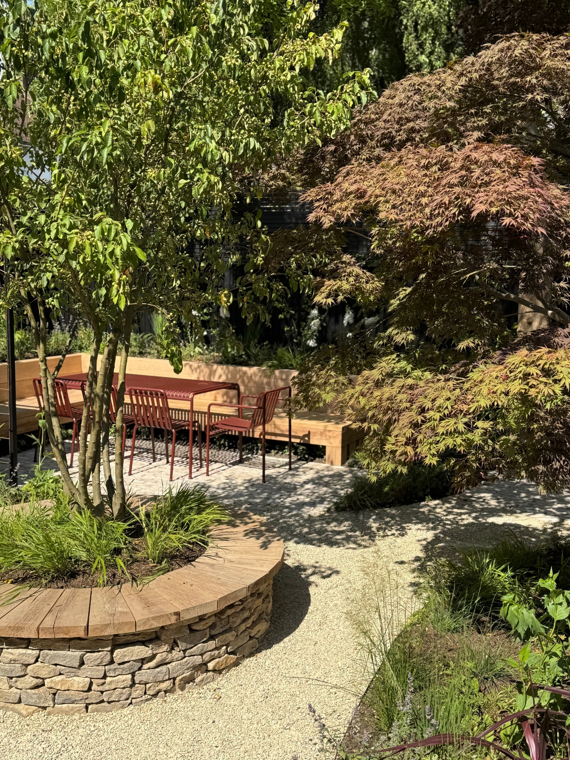 a mediterranean garden with a round planter seater, and an outdoor dining tale in red