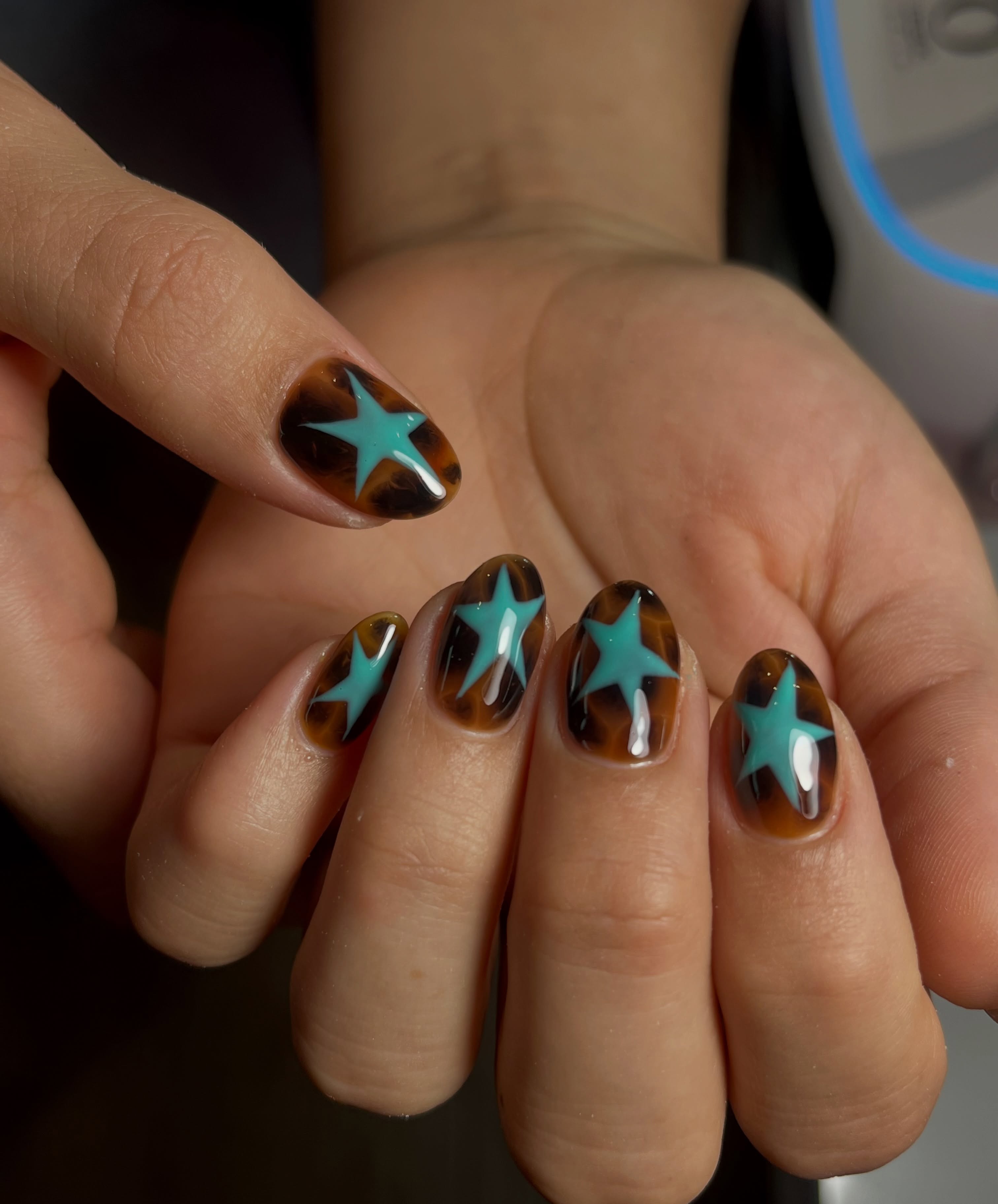 Short almond tortoiseshell nails topped with oversized turquoise star nail art