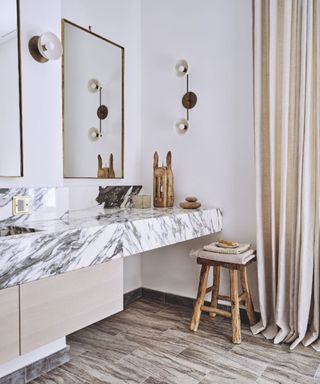 A white bathroom with a wooden stool and marble countertop