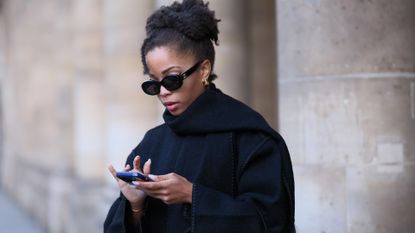 llie Delphine wears Celine sunglasses, a black oversized wool scarf, a black coat from Toteme, black cropped pants, during a street style fashion photo session, on November 06, 2023 in Paris, France. (Photo by Edward Berthelot/Getty Images)