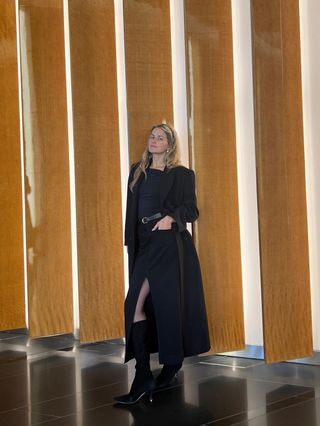 Eliza Huber wearing a black coat, black top, black denim midi skirt, and knee-high Jimmy Choo stiletto boots.