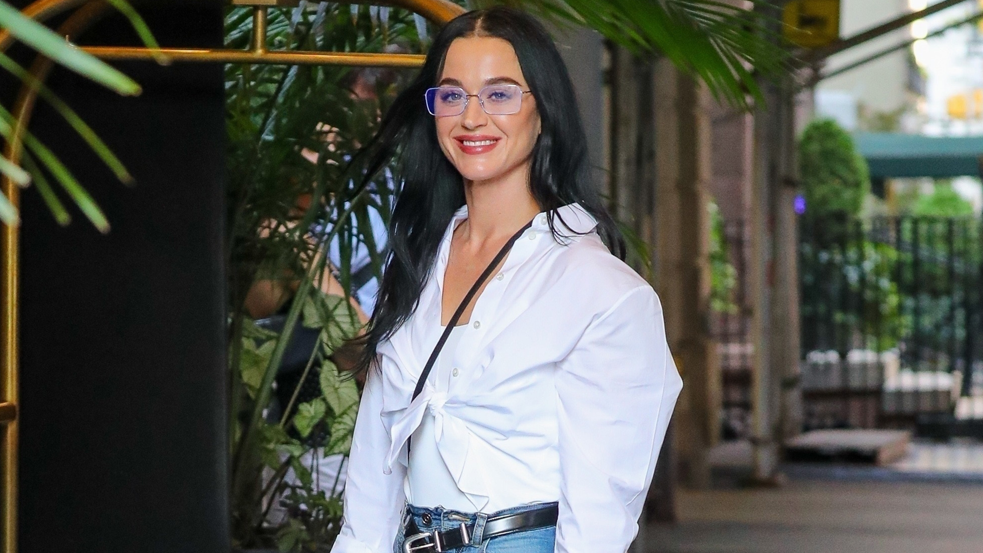 Katy Perry wears a white button down, black belt, jeans, and gucci loafers.