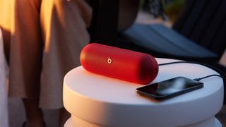 Beats Pill in Statement Red on a table, with wired USB-C audio to a smartphone