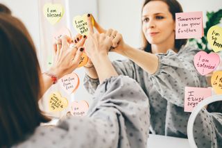 A woman attaches positive affirmations to her mirror