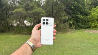 The back of the Poco F6 Pro being held in front of grass and trees