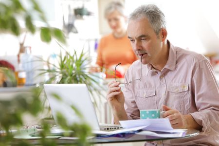 Older couple at home, man with laptop - stock photo