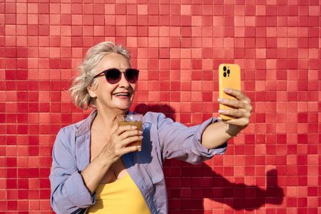 Woman taking a selfie with a drink against red tiled wall 