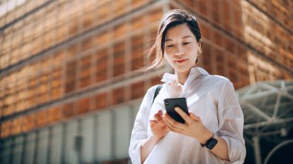 Woman looking at her phone standing outside of an office building