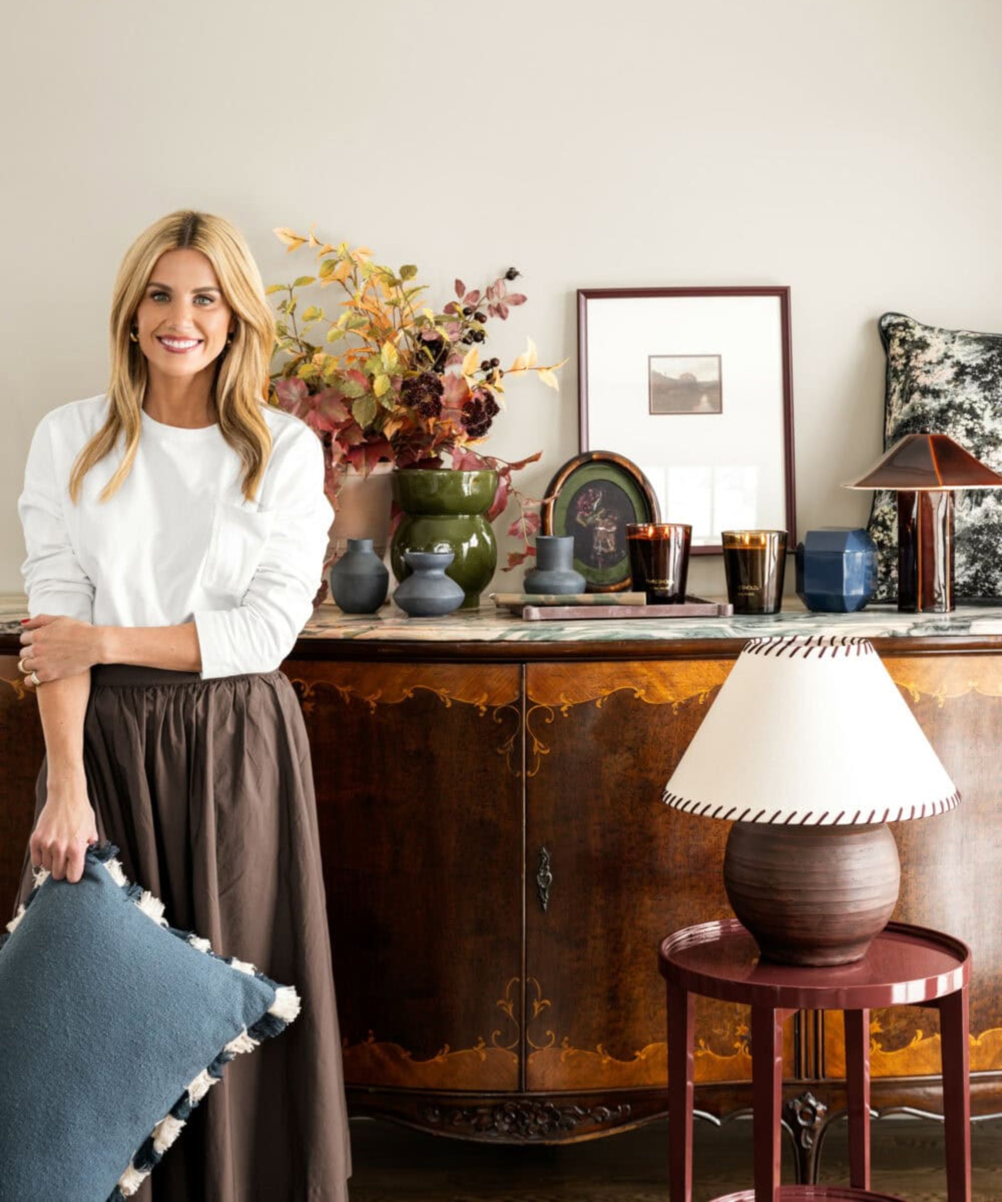 designer shea mcgee photographed for her target 2025 collection with a large dark wooden antique console styled with art, lamps, and pillows