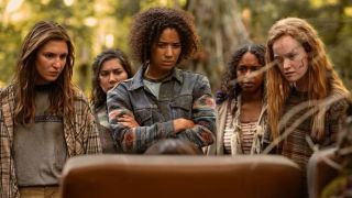 Plane crash survivors Shauna (Sophie Nélisse), Taissa (Jasmin Savoy Brown), and Vanessa (Liv Hewson) stare expectantly at an unseen person in the sunny wilderness in Yellowjackets Season 3.