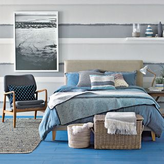 bedroom with blue wooden floor and texture wall and grey arm chair and baskets and cushions and throw