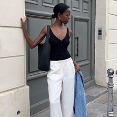 French influencer Sylvie Mus wears Mango black tank top and Mango white trousers, leaning against a door in Paris.