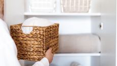 Someone putting a woven basket of folded towels back into a white linen closet