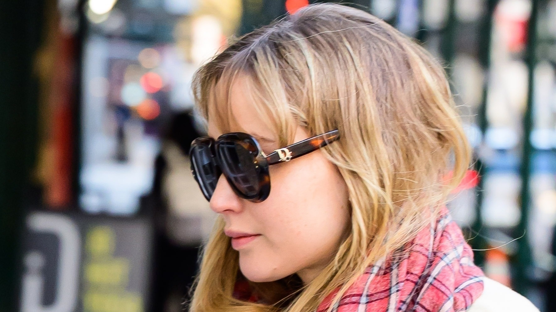 Jennifer Lawrence wearing a pale yellow coat, colorful scarf, La Ligne pants, Nike sneakers, and Dior sunglasses.