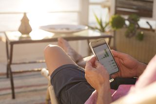 Man checking financial trading data on mobile phone while relaxing on terrace