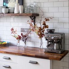 A white tiled kitchen with floral decor and a coffee machine