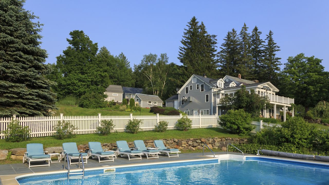 Pool against a backdrop of a white picket fence and a large country house