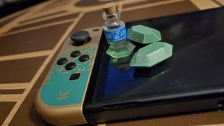 Close up of the left Joy-Con of the Tears of the Kingdom Nintendo Switch OLED model with replicas of items from the Zelda game sitting on top.