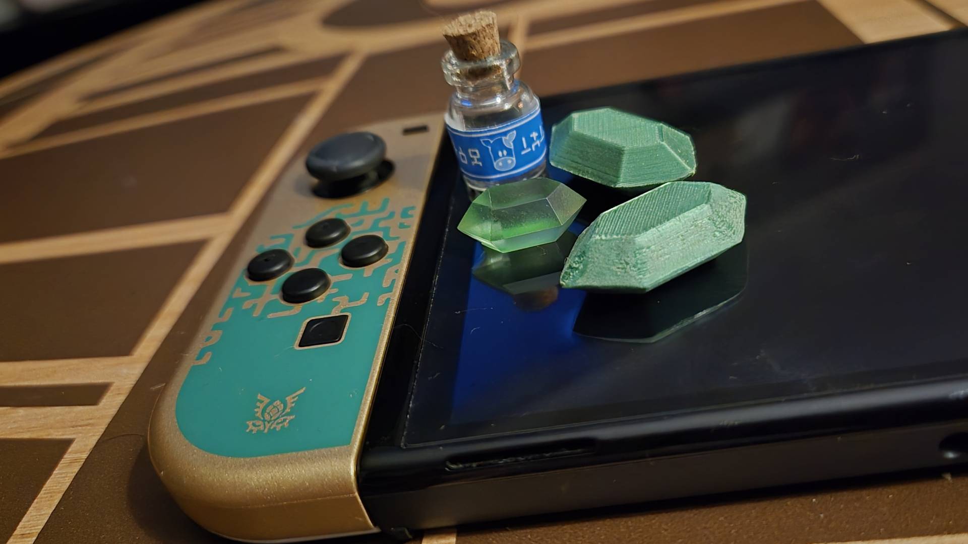 Primer plano del Joy-Con izquierdo de Tears of the Kingdom del modelo OLED de Nintendo Switch con réplicas de los elementos del juego Zelda encima.