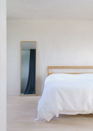 minimalist bedroom with white bedding and rectangular mirror