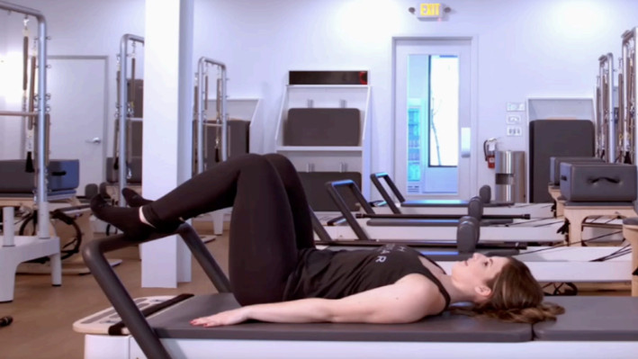Woman on a Reformer Pilates machine demonstrating an exercise
