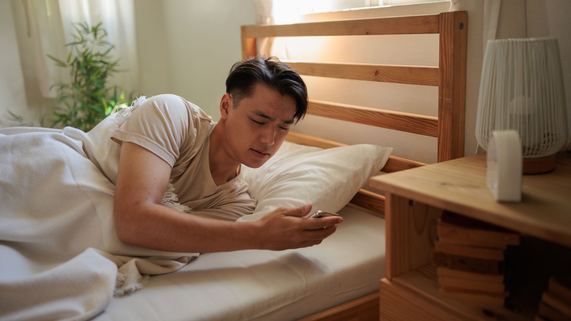 A man appears groggy as he looks at his phone in bed after waking up.